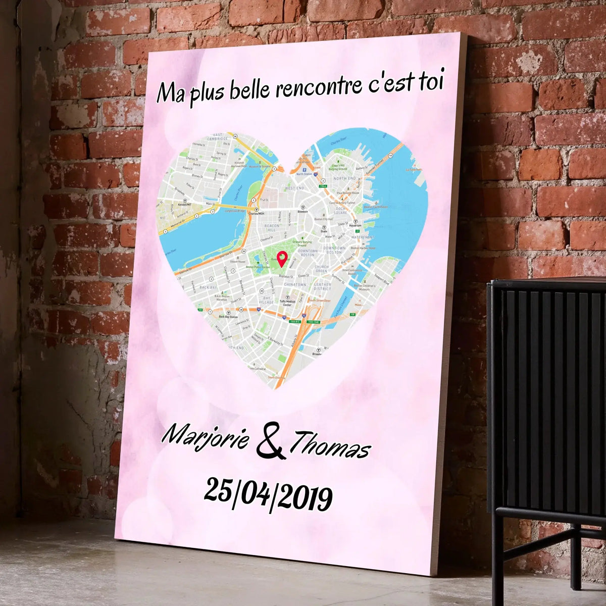 Affiche personnalisée maps style cœur posée au sol sur mur de briques rouges, entourée de cadres