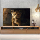 Tableau Décoratif Lion de la Grotte en verre acrylique, posé sur un meuble TV en bois devant un mur en béton