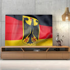 Tableau Drapeau Allemagne en verre acrylique, posé sur un meuble TV en bois devant un mur en béton