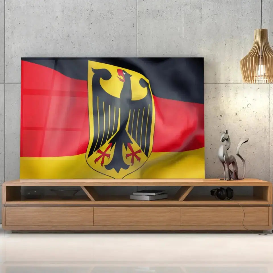 Tableau Drapeau Allemagne en verre acrylique, posé sur un meuble TV en bois devant un mur en béton