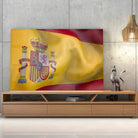 Tableau Drapeau Espagne en verre acrylique, posé sur un meuble TV en bois devant un mur en béton