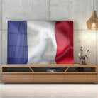 Tableau Drapeau France en verre acrylique, posé sur un meuble TV en bois devant un mur en béton