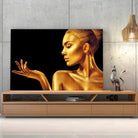 Tableau Femme glamour en or sur toile, posée sur un meuble TV en bois devant un mur en béton