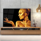 Tableau Femme glamour en or en verre acrylique, posé sur un meuble TV en bois devant un mur en béton