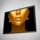 Tableau Femme maquillage en or en affiche dans un cadre noir, vue inclinée sur un mur gris