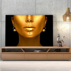 Tableau Femme maquillage en or sur toile, posée sur un meuble TV en bois devant un mur en béton
