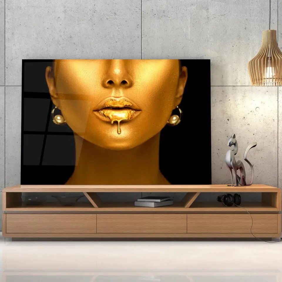 Tableau Femme maquillage en or en verre acrylique, posé sur un meuble TV en bois devant un mur en béton