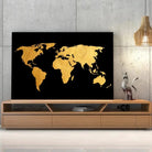 Tableau Décoratif Map Monde Fond Noir sur toile, posée sur un meuble TV en bois devant un mur en béton