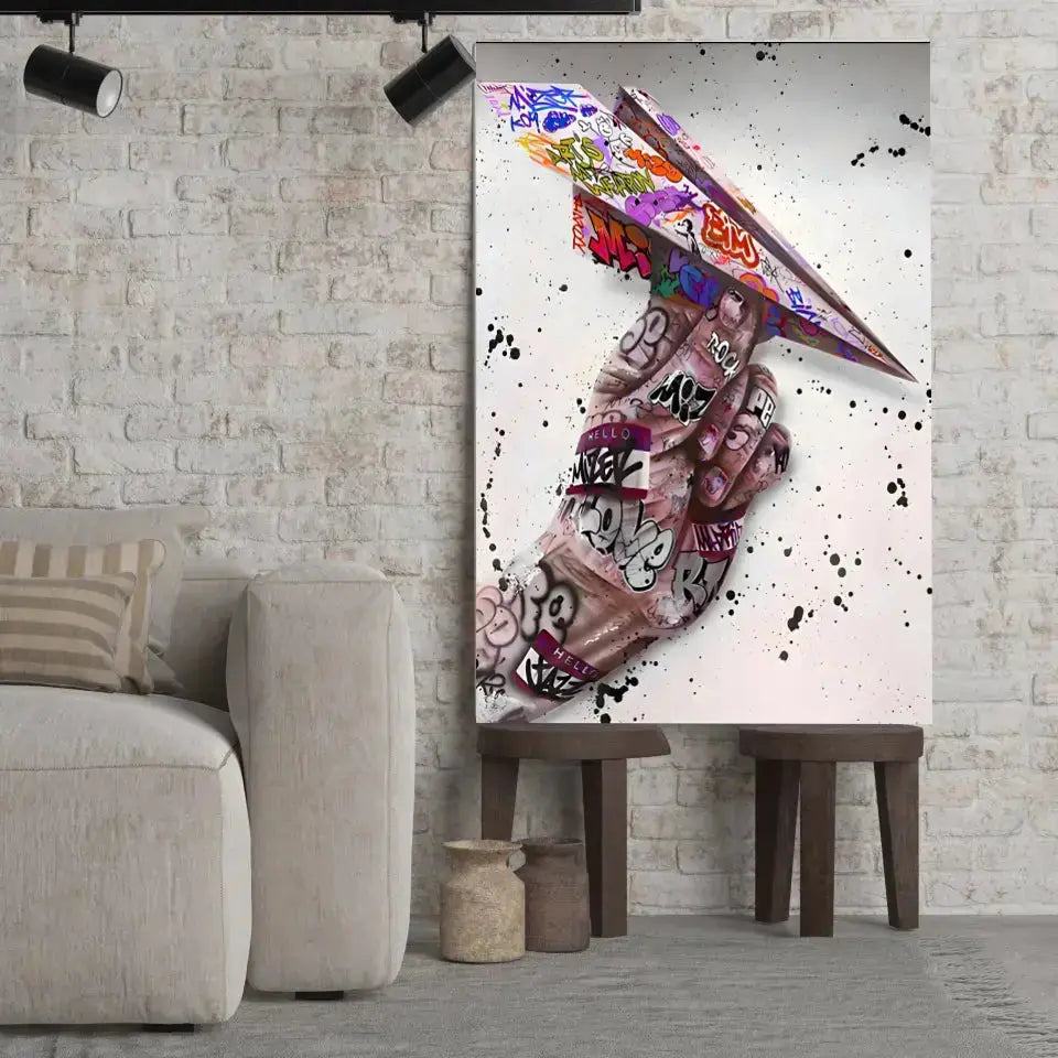 Tableau Street Art Avion en Papier sur toile, posé sur des tabourets devant un mur de briques