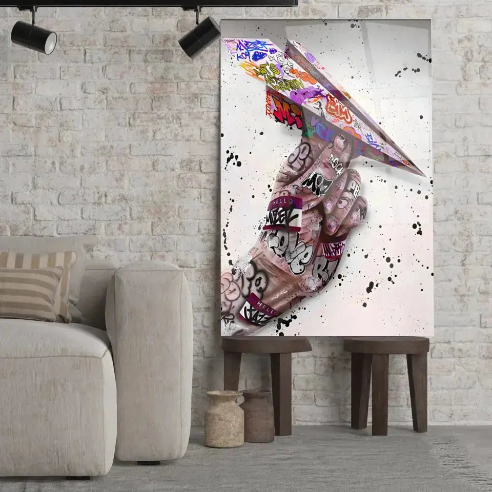 Tableau Street Art Avion en Papier en verre acrylique, posé sur des tabourets devant un mur de briques