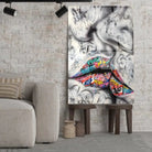 Tableau Street Art Baiser Urbain en verre acrylique, posé sur des tabourets devant un mur de briques