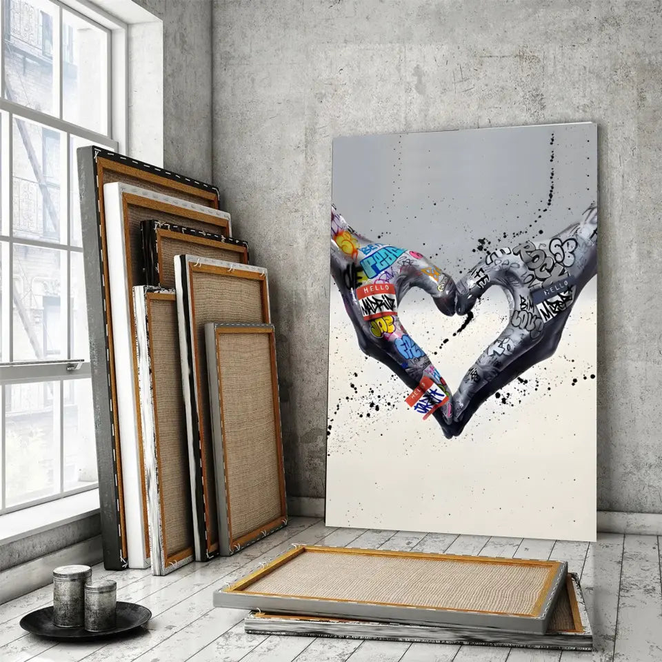 Tableau Street Art Cœur Créatif sur toile, posé devant des cadres empilés près d'une fenêtre