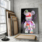 Tableau Street Art Kaws Bearbrick sur toile, posé devant des cadres empilés près d'une fenêtre