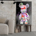 Tableau Street Art Kaws Bearbrick sur toile, posé sur des tabourets devant un mur de briques