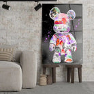 Tableau Street Art Kaws Bearbrick en verre acrylique, posé sur des tabourets devant un mur de briques