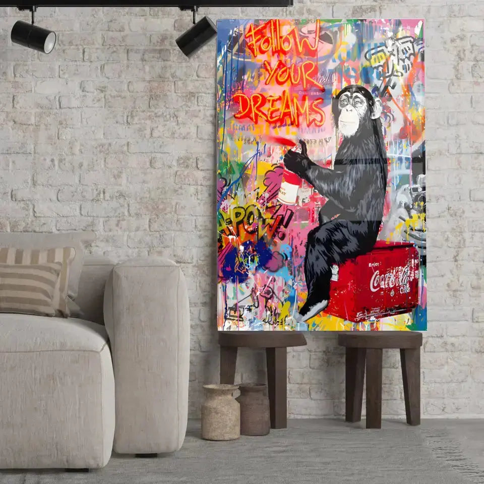 Tableau Street Art Pause Urbaine en verre acrylique, posé sur des tabourets devant un mur de briques