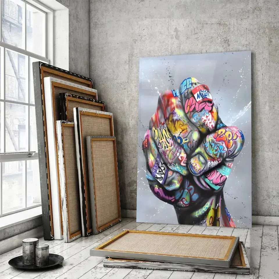 Tableau Street Art Poing de Révolte en verre acrylique, posé devant des cadres empilés